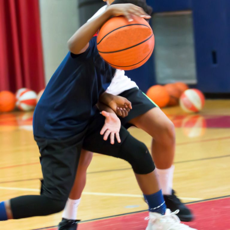 Two teenage male basketball players doing a one on one drill indoors at a local basketball camp over the summer.